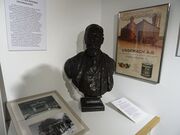 buste de Léon Ungemach et à l'arrière plan à droite, panneau publicitaire de ses produits